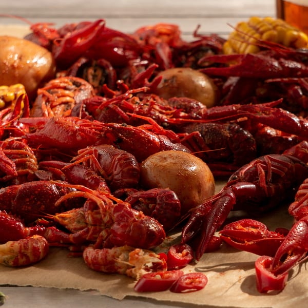 Boiled red crawfish, corn on the cob, potatoes, and chili peppers on brown paper.