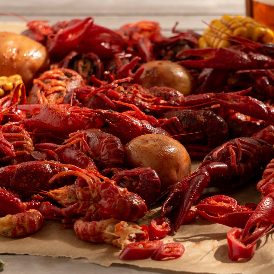 Boiled red crawfish, corn on the cob, potatoes, and chili peppers on brown paper.